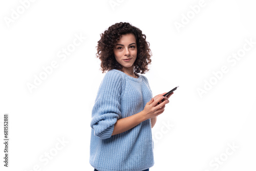 young pretty lady with black curly hair dressed in a light blue sweater is chatting on a smartphone