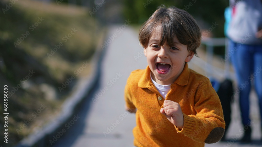 Joyful excited little boy running outside during autumn day wearing yellow pullover. Close-up face of child in motion sprinting forward feeling carefree