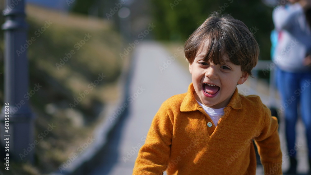 Joyful excited little boy running outside during autumn day wearing yellow pullover. Close-up face of child in motion sprinting forward feeling carefree