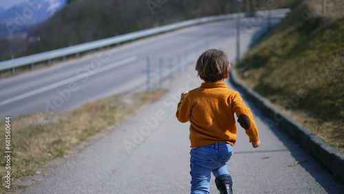 From behind, a spirited child in a yellow pullover, jeans, and boots sprints with delight through the autumn scenery. The lively run embodies the thrill of the crisp fall air