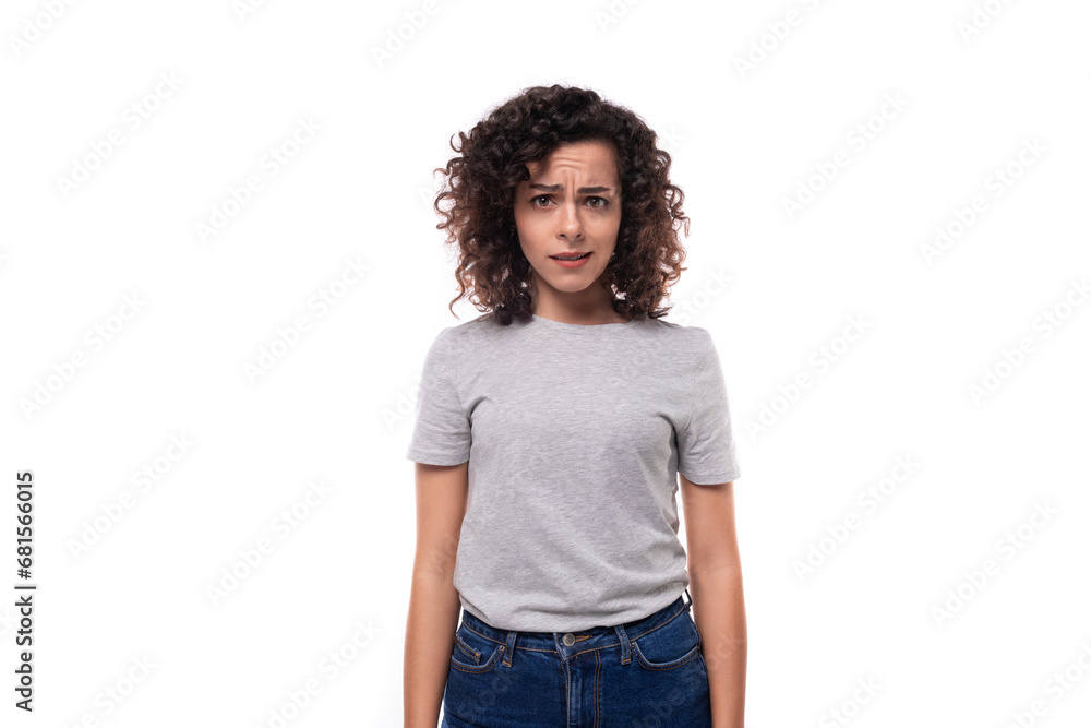 upset slender curly brunette promoter woman with glasses is dressed in a gray basic t-shirt on a white background with copy space upset slender curly brunette promoter woman with glasses is dressed in a gray basic t-shirt on a white background with copy space