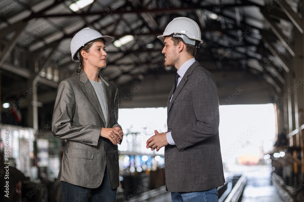 business man and woman standing together talking in heavy industry locomotive shop building site.