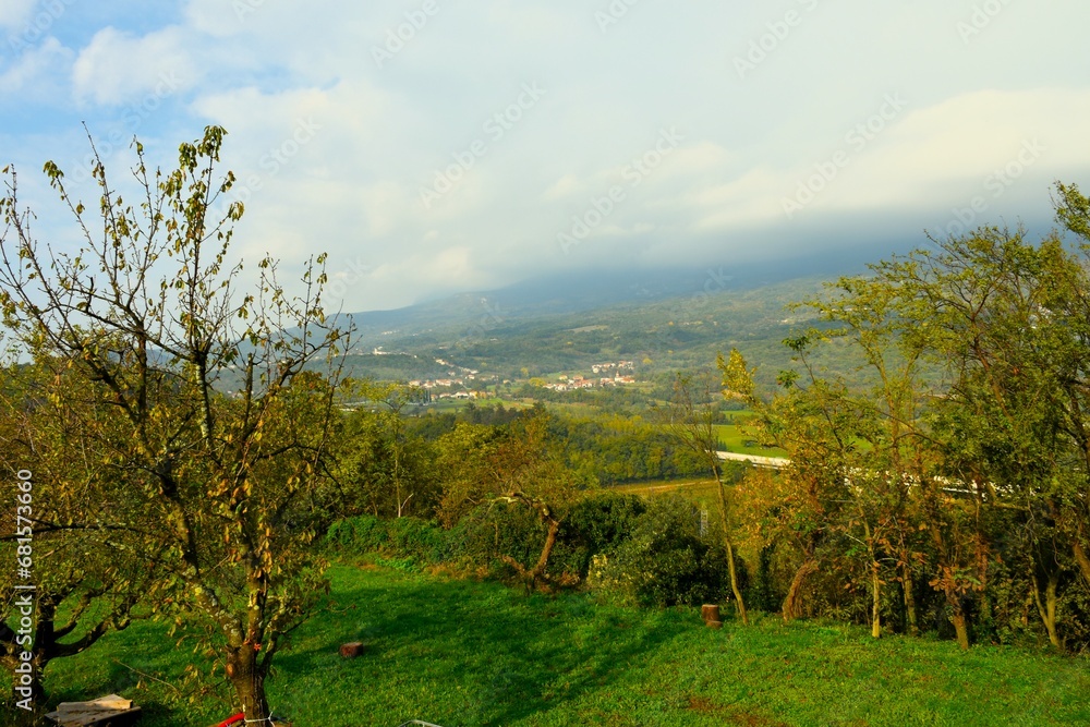 View of Vipava valley and Skrilje village lit by sunlight with the hills above covered in clouds in Primorska, Slovenia