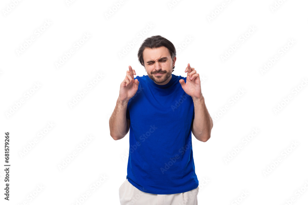 young brunette man with a beard dressed in a blue t-shirt crossed his fingers in hope on a white background young brunette man with a beard dressed in a blue t-shirt crossed his fingers in hope on a white background