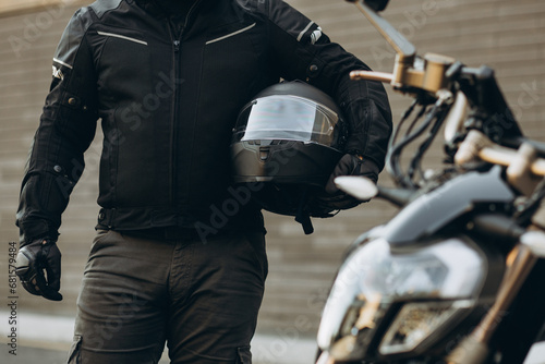 Man biker standing by his motorbike holding his helmet