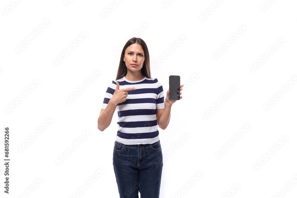 attractive young caucasian brunette woman in a striped t-shirt demonstrates the screen of a smartphone on a white background with copy space attractive young caucasian brunette woman in a striped t-shirt demonstrates the screen of a smartphone on a white background with copy space