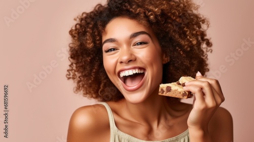 Smiling young woman savoring a cookie in a studio scene.