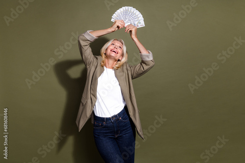 Photo of profitable business concept experienced old successful woman raised income dollars above head isolated on khaki color background