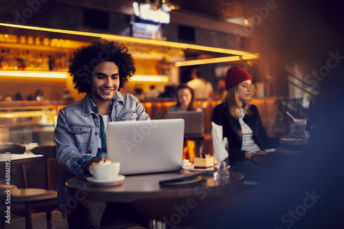 Young man sitting in cafe and using laptop photo