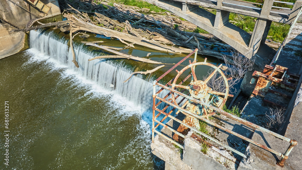 Rusty wheel equipment and railing of Maumee River Dam choked by logs above waterfall Fort Wayne, IN aerial