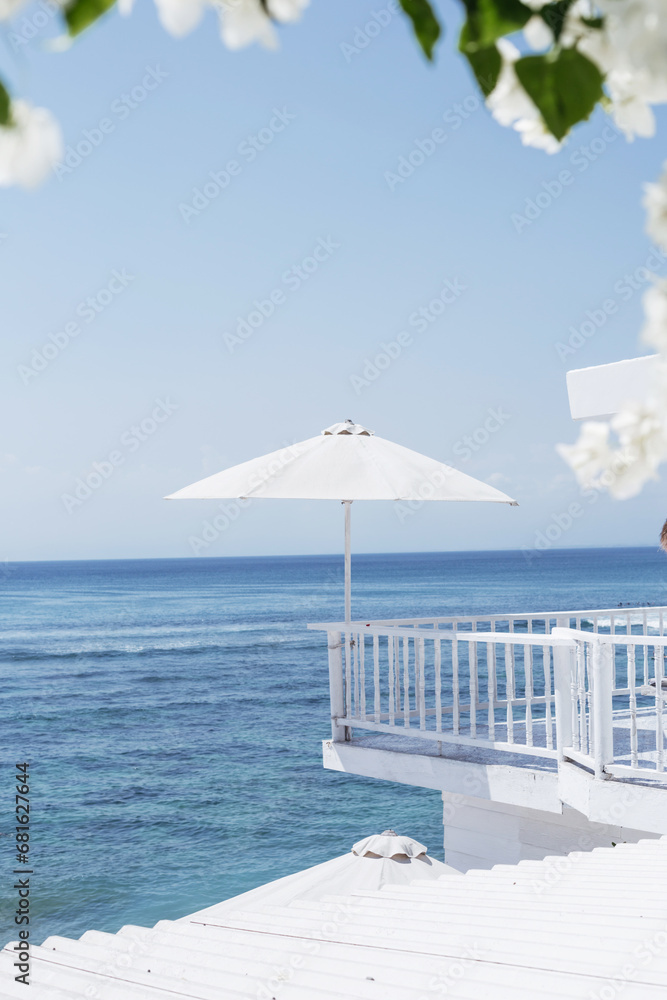 Fototapeta premium A large white umbrella on the background of the blue ocean. Stylish concept of beach holidays and resorts. Beautiful view from the hotel while traveling