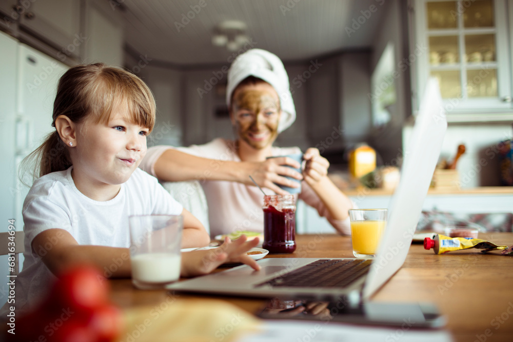 Little girl using laptop during breakfast in the kitchen with mother Little girl using laptop during breakfast in the kitchen with mother