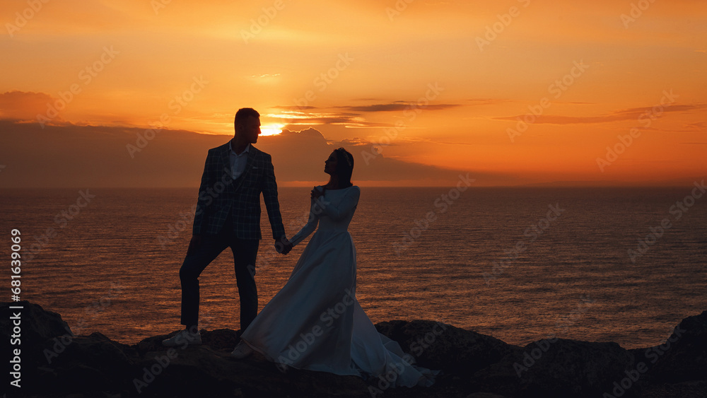 Portrait of a beautiful bride and groom at sunset in Cyprus. Young couple on a background of sea and orange sky. Wedding and love concept.