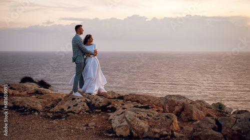 Gentle young wedding couple, bride and groom, hugging and enjoying the view on a rocky beach near the sea in evening Cyprus. Beautiful wedding photo shoot. Wedding for two, time for two. photo