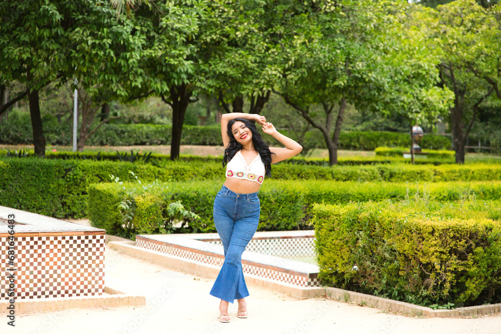 Fototapeta premium Young and beautiful Latin woman from South America walks among the trees and vegetation of the park. The woman is smiling and happy and is posing for photos. Travel and holiday concept.