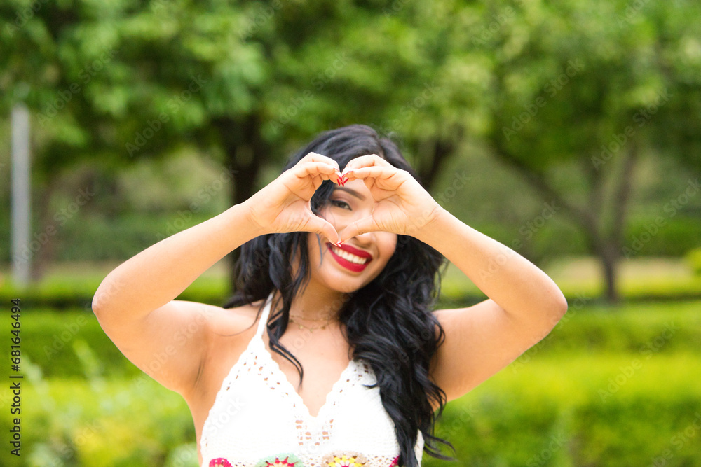 Young and beautiful brunette woman and latin, making a heart shape with her hand and fingers smiling looking through the sign. Concept friendship and love. 14 of february valentine's day. Young and beautiful brunette woman and latin, making a heart shape with her hand and fingers smiling looking through the sign. Concept friendship and love. 14 of february valentine's day.