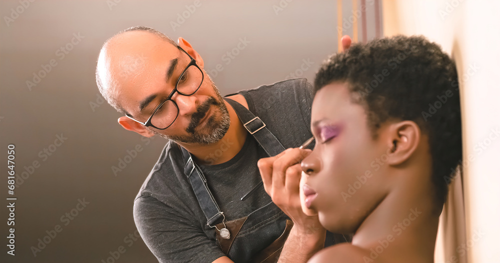 Fototapeta premium Bearded makeup artist applying eyeshadow on black transgender model
