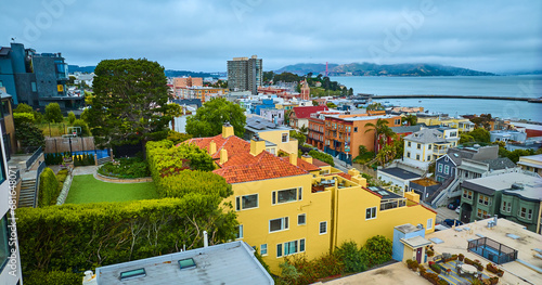 Bright yellow San Francisco apartment building with green roof and distant Aquatic Cove aerial, CA photo