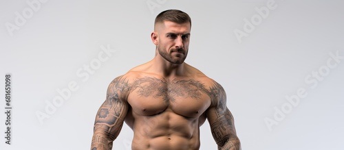 In the isolated white background, a young adult man with a muscular and tattooed torso stands, exuding power and strength, showcasing the beauty of his athletic body, evoking a sense of health and a photo