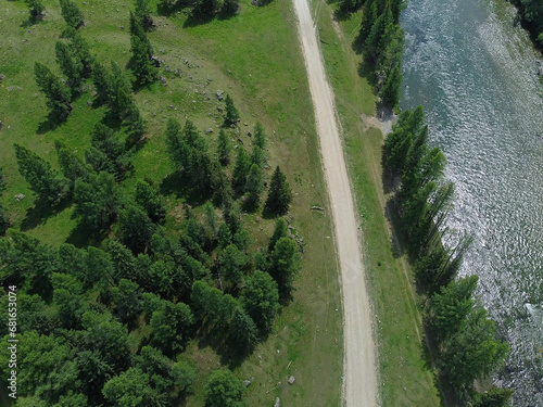 Aerial view of a green mountain landscape and alpine meadows where a river flows from the mountains and a beautiful coniferous forest stretches.