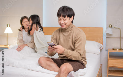 Asian husband sitting on bed in bedroom at home at night, hiding, unfaithfully cheating on his wife, using mobile phone to chat with another woman. Family, marriage issue or problem Concept. photo