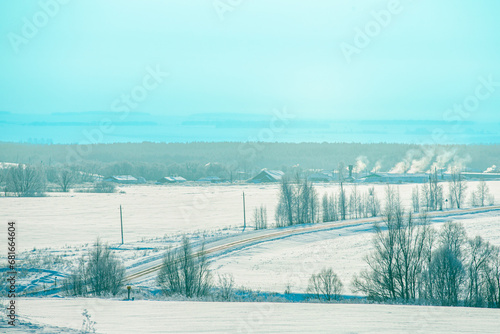 Serpentine road to the village in winter. Smoke comes out of the chimneys above the village houses. Rural landscape