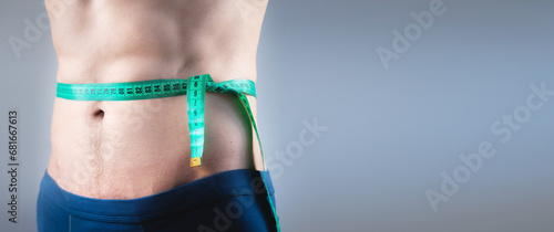 Close-up of an athlete measuring body fat with a centimeter on a gray background. A man lost weight thanks to a diet and pumped up his abs  photo for banner