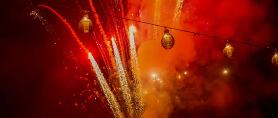 Bright red and orange fireworks against dark sky with lanterns during Chinese lunar new year celebration