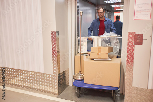 Man pushing cart with furniture and boxes when walking out of elevator in self-facility unit
