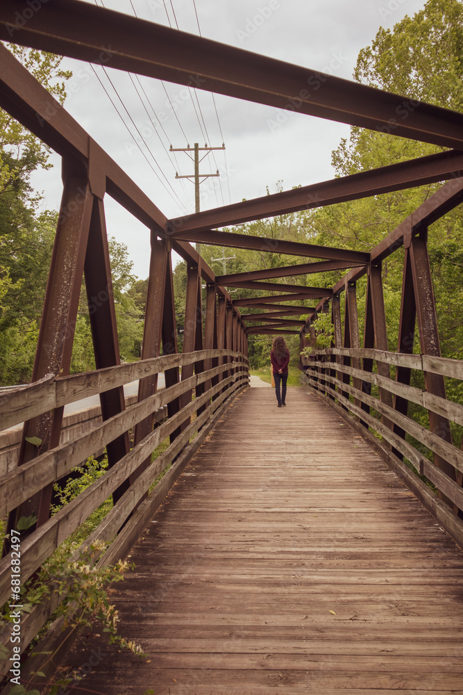 Walking into the future - a person walking away from the camera across a boardwalk footbridge in a nature area