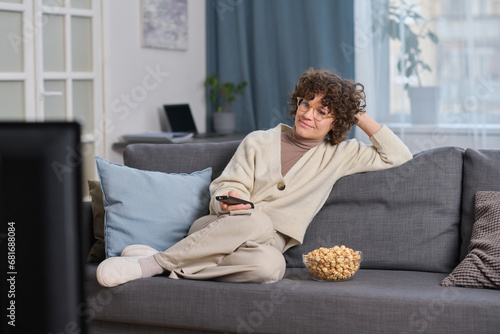Young woman watching TV in the living room while sitting on sofa with popcorn