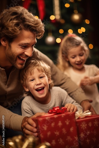 little boy opening pile of presents and smiling with excitement while his fam...