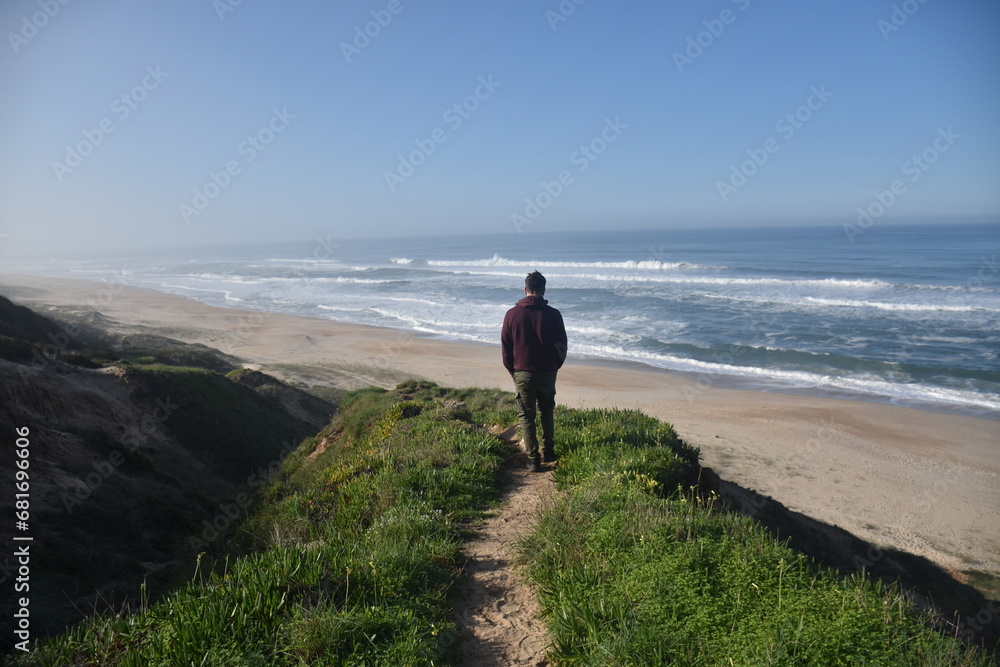 a boy walking on a natural cliff path with the beach in the background
