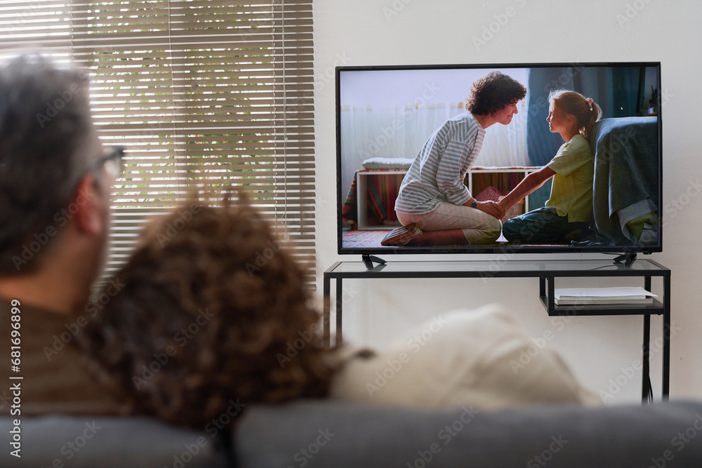 © Mediaphotos - Rear view of couple sitting on sofa and embracing while watching movie together at home © Mediaphotos - Rear view of couple sitting on sofa and embracing while watching movie together at home