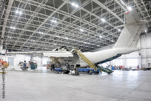 White transport aircraft in the aviation hangar. Airplane under maintenance. Checking mechanical systems for flight operations