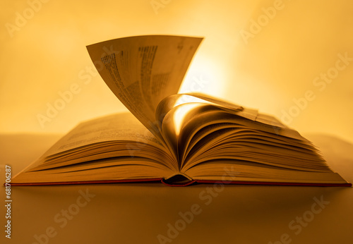 In backlighting, the pages of a large book are turned up close to the front to emphasise the sinuous movement of the pages. Intense bokeh. Warm atmosphere. Copy space.