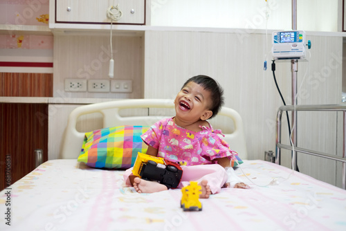 2-year-old baby in pink patient uniform Lying laughing, smiling in a hospital bed.