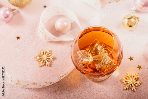 Glass of whiskey or bourbon with festive Christmas decoration on light beige background. New Year, Christmas and winter holidays whiskey mood concept