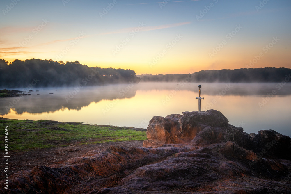 Excalibur l'épée légendaire du roi Arthur,  plantée sur son rocher devant un étang dans la brume du matin au lever du soleil en forêt de Brocéliande - obrazy, fototapety, plakaty 