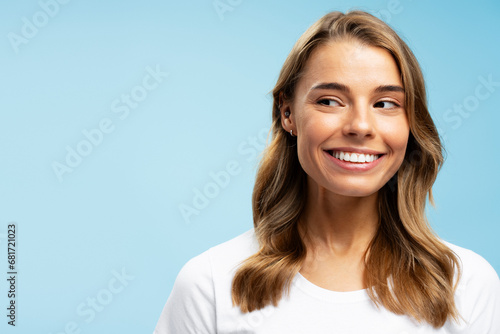 Closeup portrait beautiful smiling young woman with white healthy teeth and stylish wavy hair looking away isolated on blue background, copy space. Health care, dental treatment concept