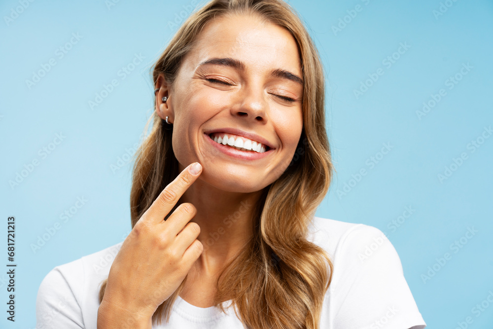 Fototapeta premium Closeup portrait smiling beautiful woman pointing finger on white teeth isolated on blue background. Advertisement, health care dental concept