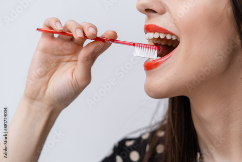 A woman brushing her teeth with a red toothbrush. A Woman Engaging in Oral Hygiene with a Vibrant Red Toothbrush