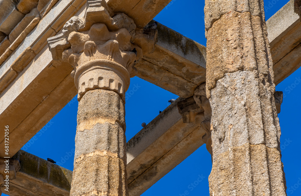 Detail of the ornate moldings on the Corinthian order columns and capitals of the well-preserved Roman Temple of Diana under a clear blue sky and doves perched on its beams. Merida.