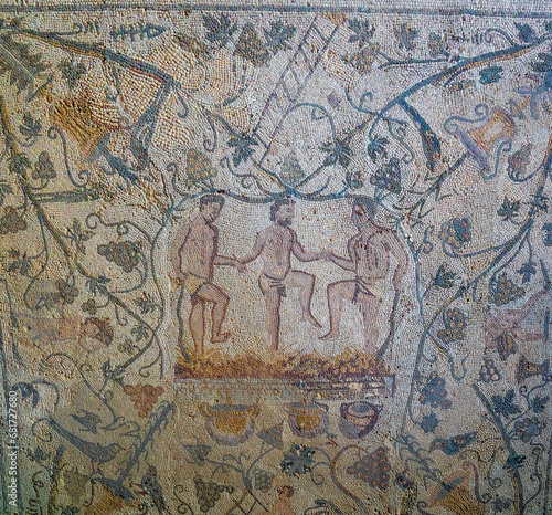 Archaeological remains of a Roman mosaic of three men in loincloths holding hands crushing grapes to make wine, with vines and animals as decoration. Mérida archaeological complex.