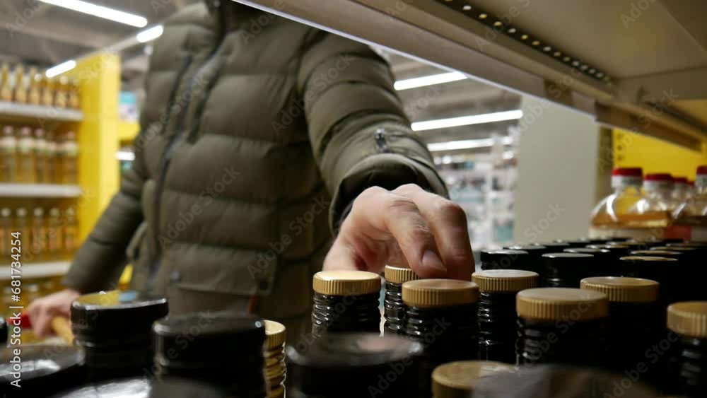 Close-up of many oil bottles on the shelf of a grocery store and a man with a shopping trolley takes two Close-up of many oil bottles on the shelf of a grocery store and a man with a shopping trolley takes two