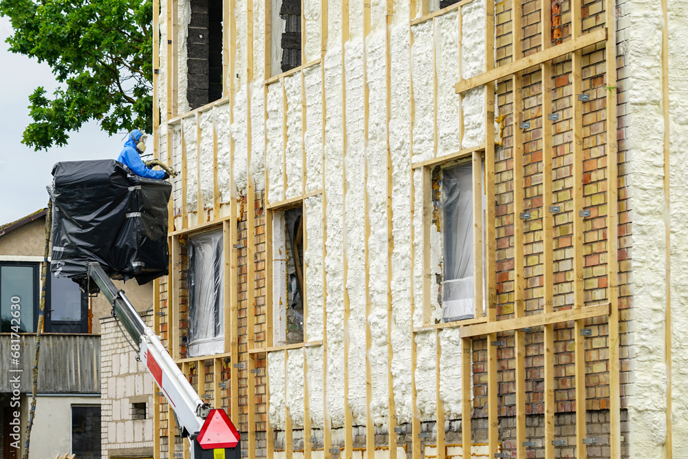 Technician spraying thermal insulation foam layer on the exterior wall using plural component gun for polyurethane foam Technician spraying thermal insulation foam layer on the exterior wall using plural component gun for polyurethane foam