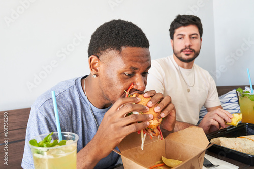Friends eating takeout food at table man taking bite of burger