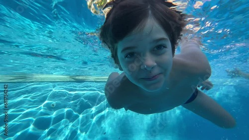 Slow motion video of happy boy of 9 years old diving and playing in the water of a swimming pool in the summer, blue water, smiling, and funny way.