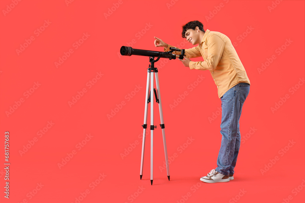 Young man looking into telescope on red background