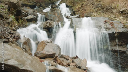 Amazing view of small rapid waterfalls running down stone boulders into a deep gorge from a steep slope. Natural beauty of mountain streams. Time Lapse. High quality 4k footage photo